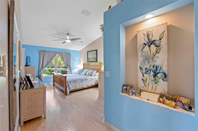 bedroom featuring ceiling fan, light wood-type flooring, lofted ceiling, and a textured ceiling