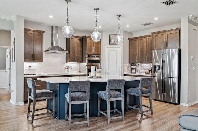 kitchen featuring hanging light fixtures, stainless steel appliances, a kitchen island with sink, and wall chimney exhaust hood