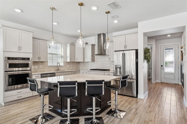 kitchen featuring stainless steel appliances, sink, wall chimney range hood, a center island, and light hardwood / wood-style floors