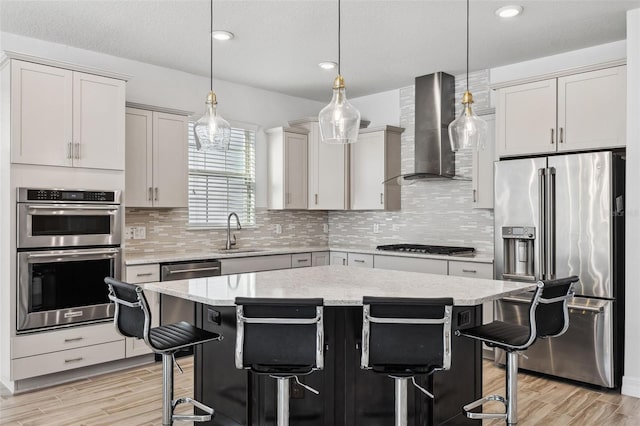 kitchen featuring a kitchen bar, wall chimney exhaust hood, stainless steel appliances, and a kitchen island