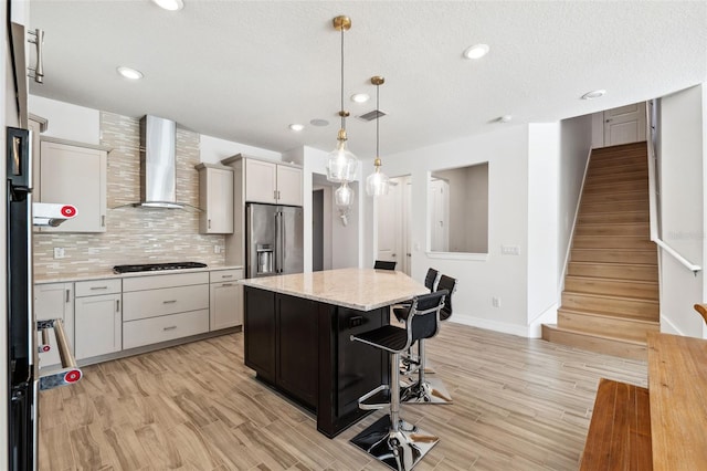 kitchen with pendant lighting, black gas cooktop, wall chimney exhaust hood, a kitchen island, and high end fridge