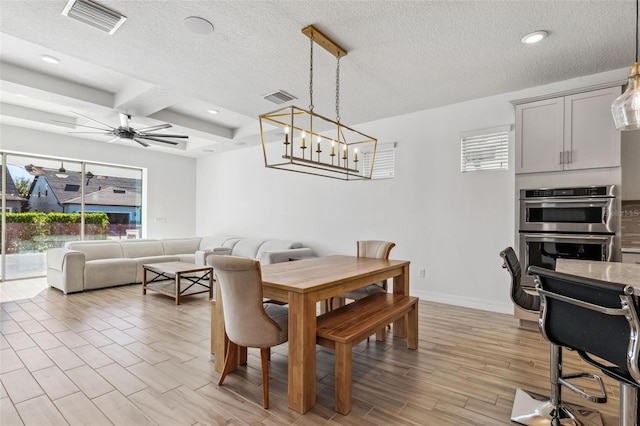 dining space featuring a textured ceiling, ceiling fan with notable chandelier, light hardwood / wood-style flooring, and coffered ceiling