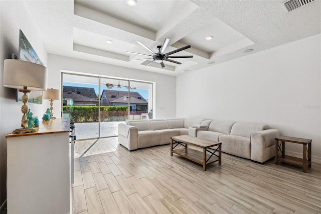 living room with a textured ceiling, light wood-type flooring, a raised ceiling, and ceiling fan