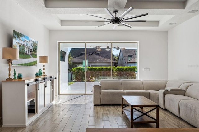 living room featuring ceiling fan, a tray ceiling, and light hardwood / wood-style flooring