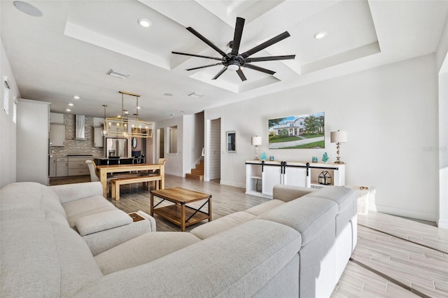 living room featuring ceiling fan, light hardwood / wood-style flooring, and a tray ceiling