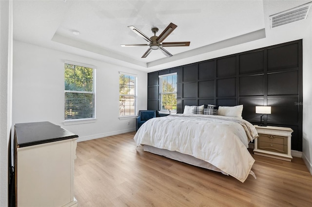 bedroom featuring ceiling fan, a raised ceiling, and light hardwood / wood-style flooring