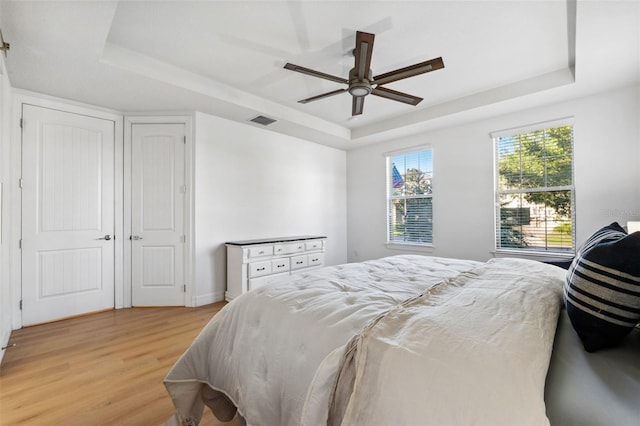 bedroom featuring a raised ceiling, ceiling fan, and light wood-type flooring