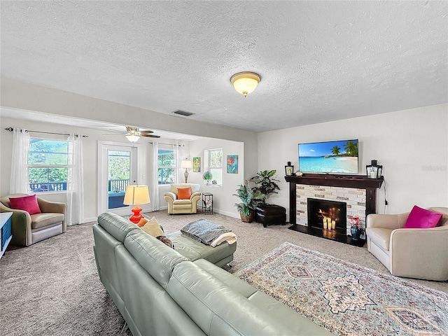 living room with a textured ceiling, ceiling fan, a fireplace, and carpet