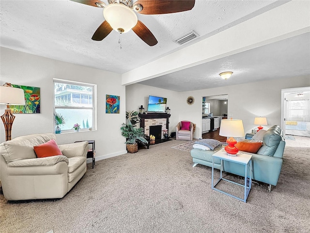 living room with carpet, a textured ceiling, ceiling fan, beam ceiling, and a stone fireplace