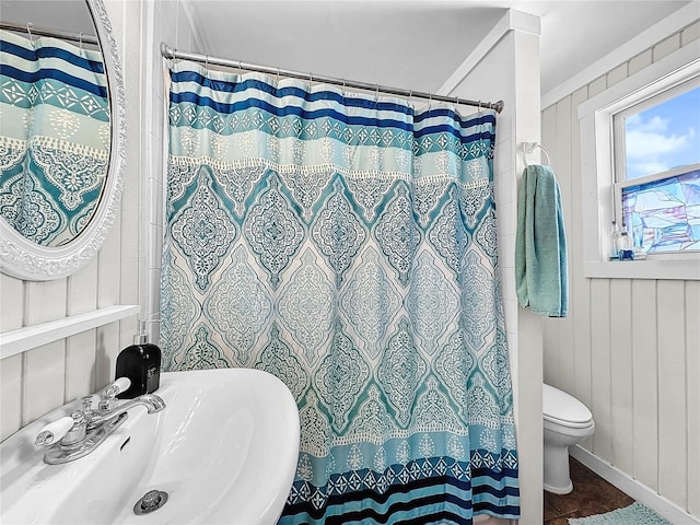 bathroom featuring a shower with shower curtain, toilet, sink, and wooden walls