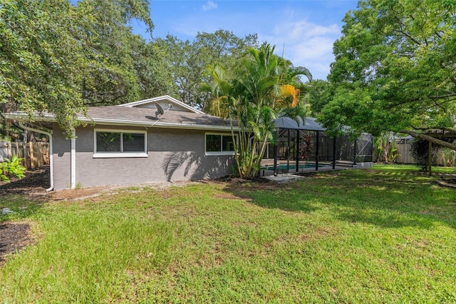 rear view of property with a fenced in pool, glass enclosure, and a lawn