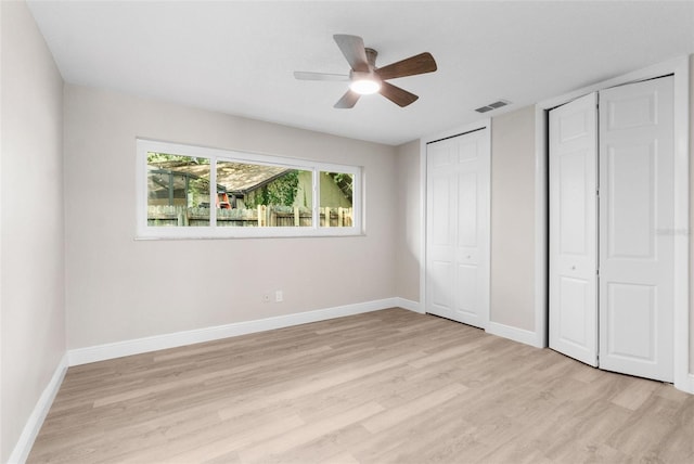 unfurnished bedroom with light hardwood / wood-style flooring, ceiling fan, and multiple closets