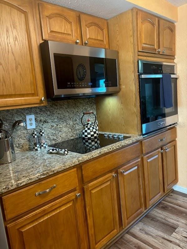 kitchen featuring appliances with stainless steel finishes, light hardwood / wood-style floors, light stone counters, and decorative backsplash