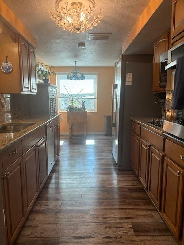 kitchen with stainless steel dishwasher, a textured ceiling, an inviting chandelier, dark hardwood / wood-style flooring, and sink