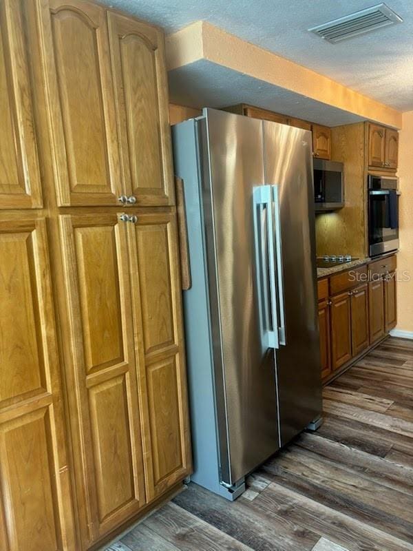 kitchen featuring a textured ceiling, black appliances, and dark wood-type flooring