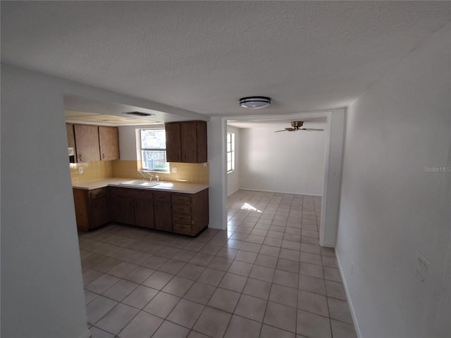 kitchen with sink, backsplash, light tile patterned floors, ceiling fan, and a textured ceiling