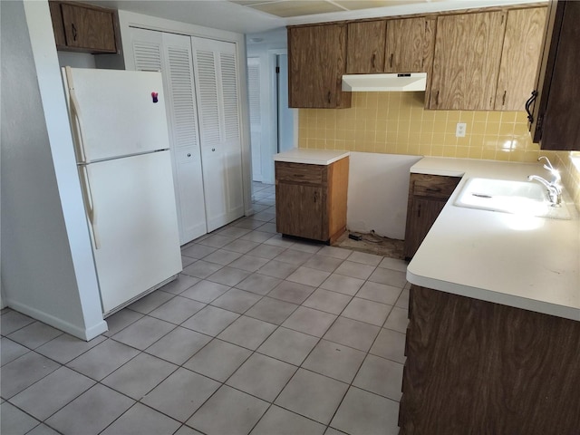 kitchen featuring white refrigerator, light tile patterned floors, sink, and backsplash