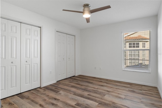 unfurnished bedroom featuring ceiling fan, wood-type flooring, and two closets