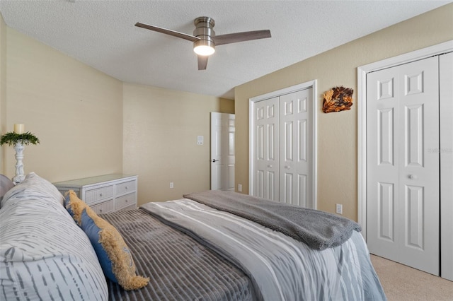 carpeted bedroom with a textured ceiling, ceiling fan, and two closets