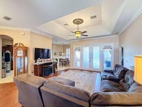 living room featuring french doors, a tray ceiling, light hardwood / wood-style flooring, and ceiling fan