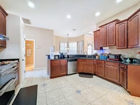 kitchen with kitchen peninsula, appliances with stainless steel finishes, sink, light tile patterned floors, and hanging light fixtures