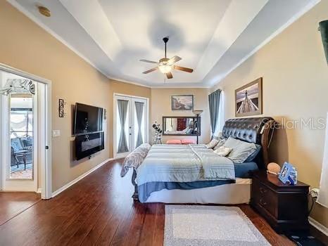 bedroom with ceiling fan, dark hardwood / wood-style floors, a raised ceiling, and french doors