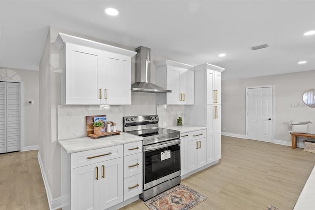 kitchen with light hardwood / wood-style floors, white cabinetry, stainless steel electric range oven, and wall chimney range hood