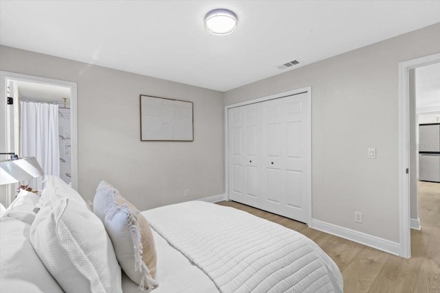 bedroom with stainless steel refrigerator, ensuite bath, a closet, and light wood-type flooring