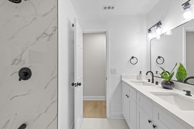 bathroom with hardwood / wood-style flooring, vanity, and a tile shower