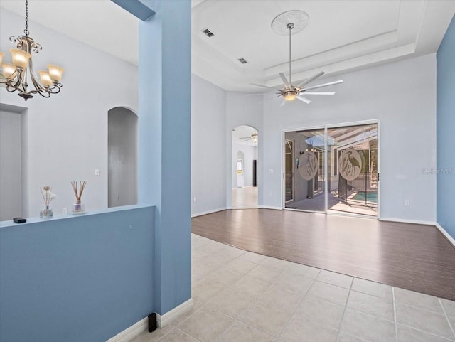 interior space with ceiling fan with notable chandelier, a raised ceiling, and light hardwood / wood-style flooring