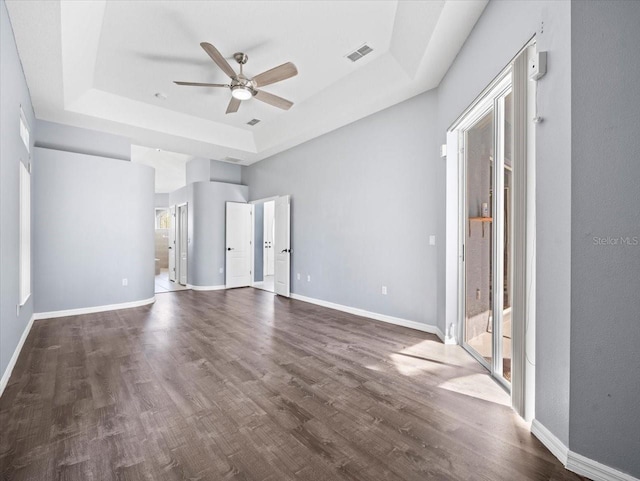 interior space featuring a tray ceiling, multiple windows, ceiling fan, and dark wood-type flooring