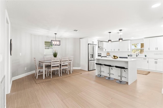 kitchen with white cabinets, hanging light fixtures, light hardwood / wood-style flooring, appliances with stainless steel finishes, and a kitchen island