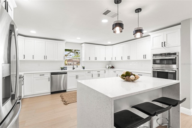 kitchen featuring pendant lighting, a center island, white cabinets, light wood-type flooring, and appliances with stainless steel finishes