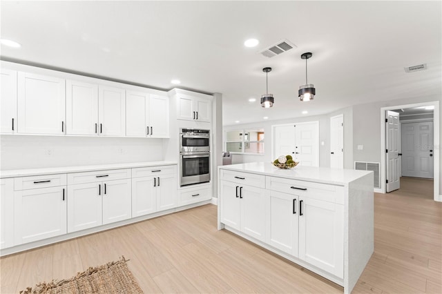 kitchen with white cabinets, decorative light fixtures, double oven, and light hardwood / wood-style floors