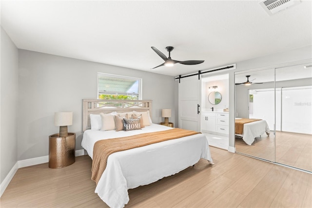 bedroom featuring connected bathroom, a barn door, ceiling fan, and light hardwood / wood-style flooring