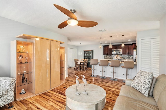 living room featuring ceiling fan, a textured ceiling, and light wood-type flooring