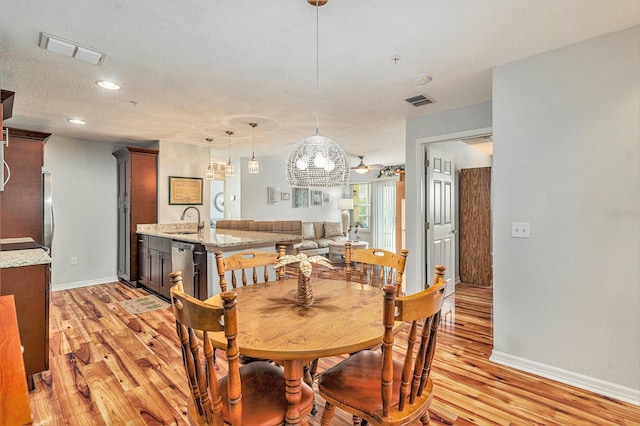 dining room with light hardwood / wood-style flooring, a chandelier, a textured ceiling, and sink