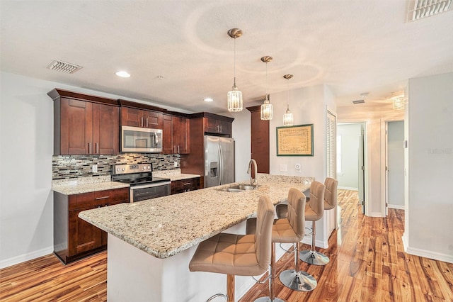 kitchen featuring sink, hanging light fixtures, light hardwood / wood-style floors, a breakfast bar area, and appliances with stainless steel finishes