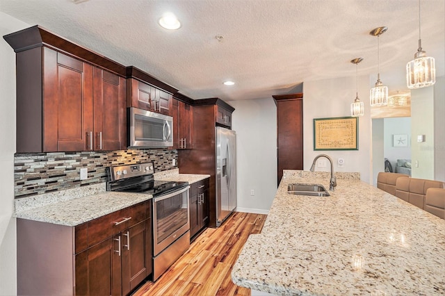 kitchen featuring light wood-type flooring, backsplash, stainless steel appliances, sink, and hanging light fixtures