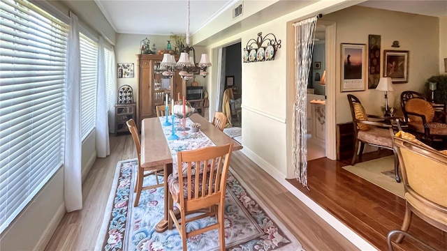 dining room featuring a notable chandelier, visible vents, wood finished floors, and ornamental molding