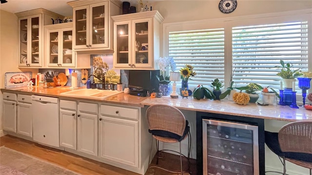 kitchen with dishwasher, sink, beverage cooler, light stone counters, and light hardwood / wood-style floors