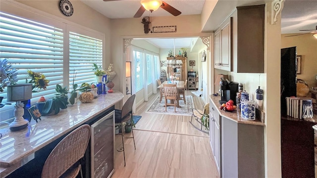 kitchen featuring ceiling fan, beverage cooler, light stone countertops, and light hardwood / wood-style floors