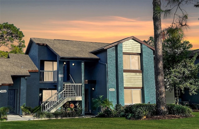 view of front of property featuring roof with shingles, stairway, a front lawn, and stucco siding