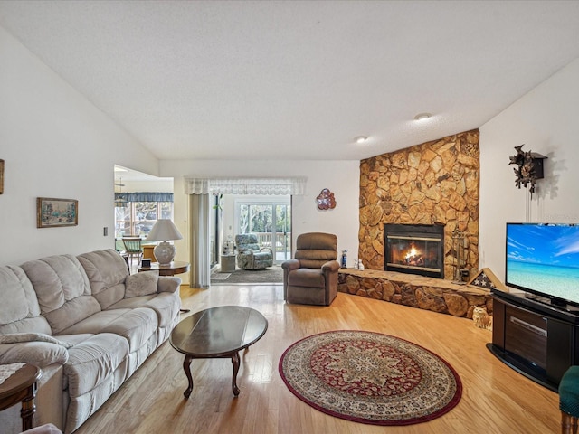 living room featuring a stone fireplace, lofted ceiling, a textured ceiling, and light hardwood / wood-style flooring