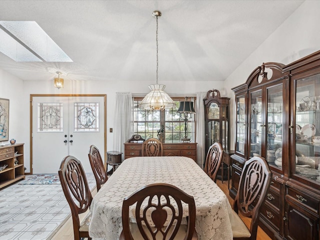 dining room with french doors, a textured ceiling, and vaulted ceiling with skylight