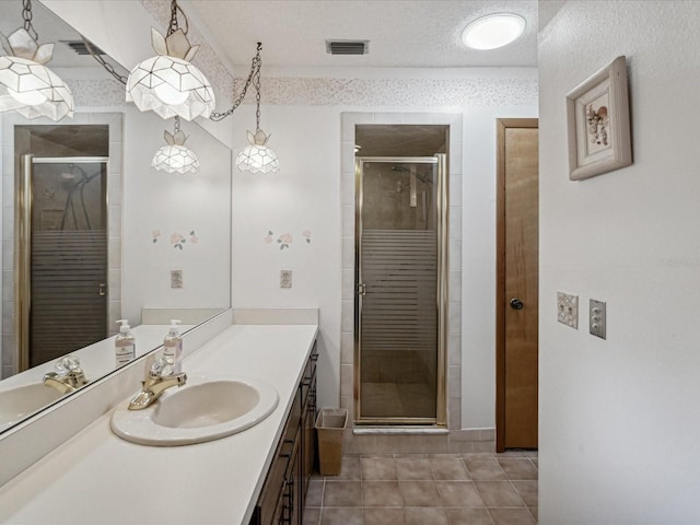 bathroom with tile patterned floors, vanity, a shower with shower door, and a textured ceiling