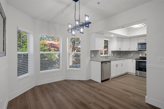 kitchen with appliances with stainless steel finishes, hardwood / wood-style flooring, hanging light fixtures, white cabinets, and decorative backsplash