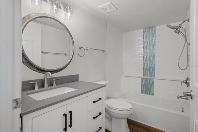 full bathroom with vanity, tiled shower / bath, toilet, and hardwood / wood-style floors