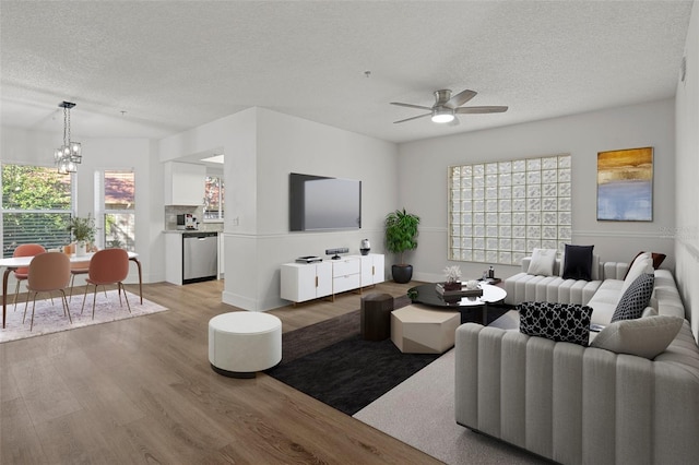 living room featuring ceiling fan with notable chandelier, light hardwood / wood-style flooring, and a textured ceiling