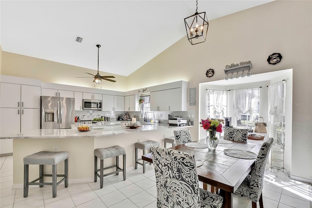 tiled dining room with ceiling fan with notable chandelier, sink, and high vaulted ceiling